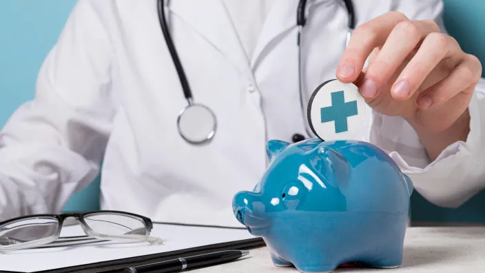 Concepto de ahorro para la salud: un doctor mete un símbolo médico en una hucha. Planificación de un seguro o gastos sanitarios.